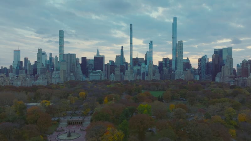 Wide panoramic view of skyscrapers surrounding Central park. Fly above autumn colour trees in park at dusk. Manhattan, New York City, USA