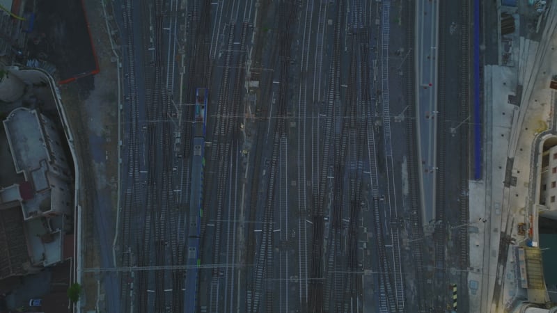 High angle view of train driving on railroad tracks. Tilt up reveal building on central train station and city at dusk. Rome, Italy