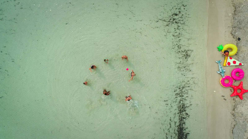 Aerial view of friends playing volleyball standing in sea by sandy beach.