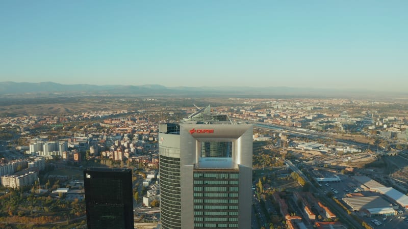 Aerial shot of top of modern skyscrapers in Cuatro Torres Business Area. Town development with housing estates, industrial and logistic site lit by afternoon sun in background.