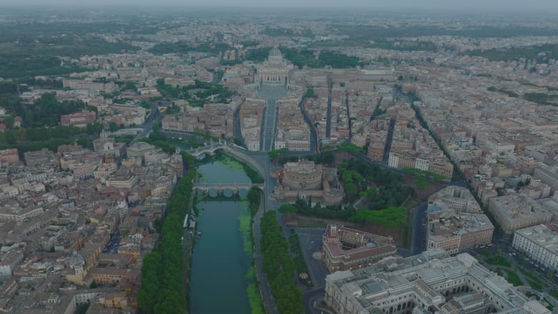 Aerial panoramic footage of Tiber river flowing through historic city centre at dusk. Castel SantAngelo on riverbank and famous St. Peters Basilica in Vatican City in distance. Rome, Italy