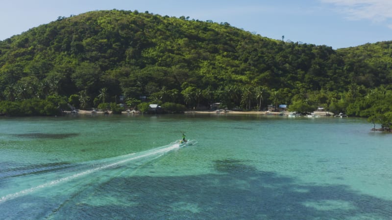 Pan of a person sailing an outrigger toward the shore of an island