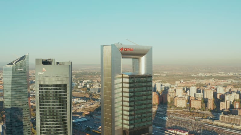 Slide and pan shot of modern high rise office buildings towering above other town development. Cuatro Torres Business area on sunny day.