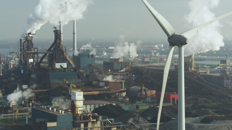 Spinning Wind Turbine Close Up With Factories and Smoke