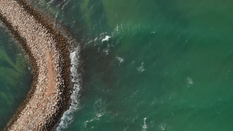 Aerial birds eye overhead top down view of breakwater barrier in Lagos, Portugal, drone flying forward reveals beautiful sandy beach coastline, day