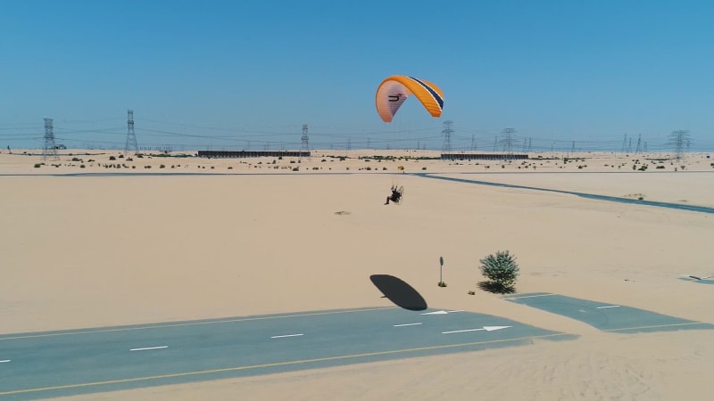 Aerial view of a man using powered parachute at desert landscape.