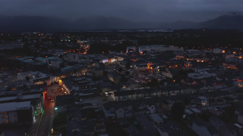 Aerial panoramic footage of town centre. Illuminated colour house facades. Lake and mountains in backgrounds. Killarney, Ireland