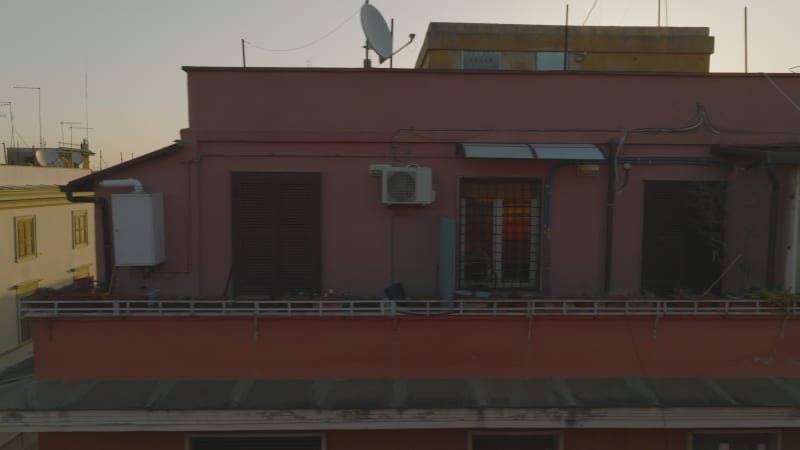 Colour facade with windows and balcony on top floor of residential building. Sliding reveal of street in city at sunrise. Rome, Italy