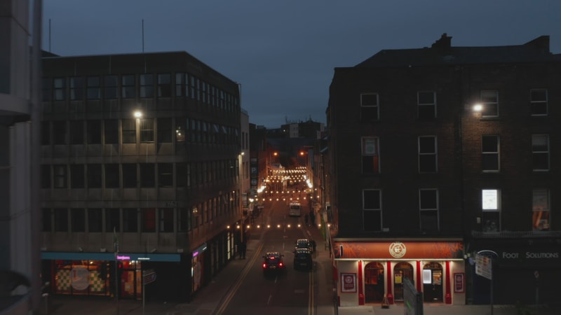 Forwards fly above illuminated narrow street in city centre. Decorative light chains across aisle. Night scene. Limerick, Ireland