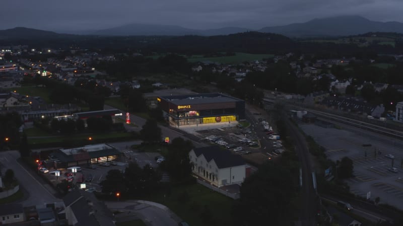 Aerial footage of glowing building at road in evening town. Modern cinema with car park. Killarney, Ireland