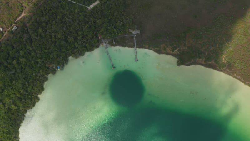 Aerial birds eye overhead top down view of colourful lake surrounded by forest. Shadow of moving clouds going through footage. Kaan Luum lagoon, Tulum, Yucatan, Mexico