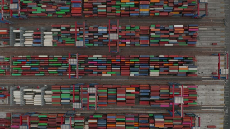 Top down birds eye aerial view of industrial cranes moving large containers in cargo port