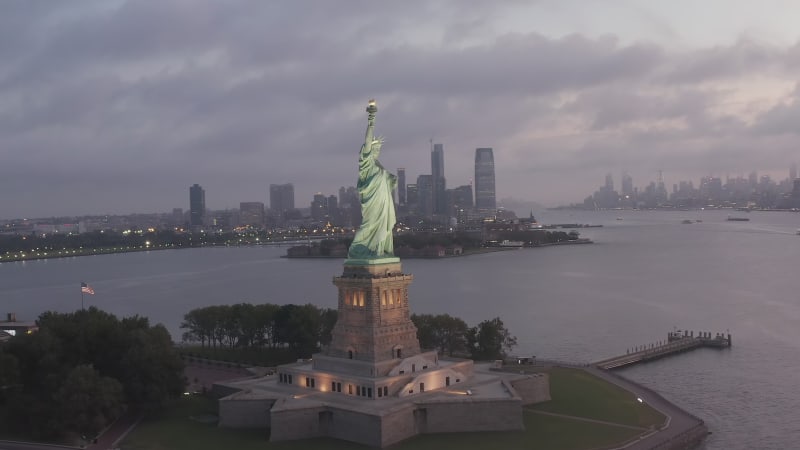 Orbit Drone Shot Around Famous Statue of Liberty revealing Manhattan Scenic Skyscraper Skyline in early Morning Sunrise, Aerial Dolly Slide left