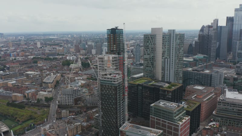 Slide and pan aerial footage of urban neighbourhood and business district. Revealing group of skyscrapers in City financial hub. London, UK