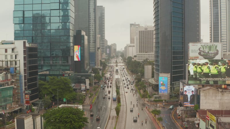 Slow flying low aerial dolly shot of dense motorway traffic in modern city center between skyscrapers in Jakarta