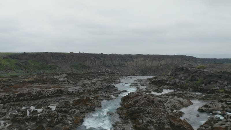 Drone view flying through water flowing on river of Skjálfandafljót with rock and basalt formations. Aerial view of Aldeyjarfoss waterfall situated in the northern part of icelandic highlands