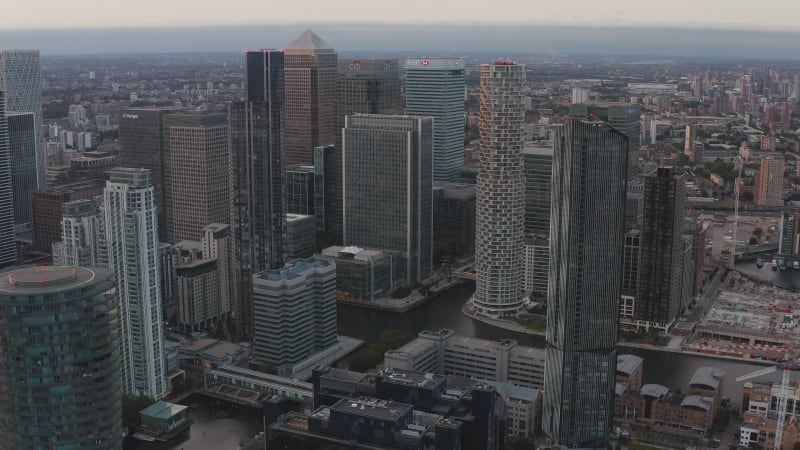 Aerial slide and pan footage of modern business urban district Canary Wharf with group of tall skyscrapers in evening. London, UK