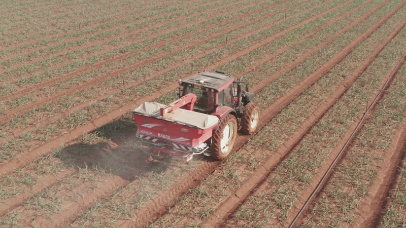 Tractor hauling a Two disc Fertilizer spreader in a large field, Aerial follow footage.