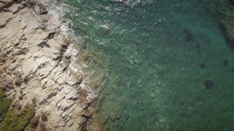 Aerial view of an empty small beach with turquoise water and stones.