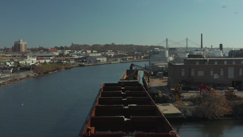 Fly over cargo ship moored at bank. Loading loose material on barge. Using transport on water in city. New York City, USA