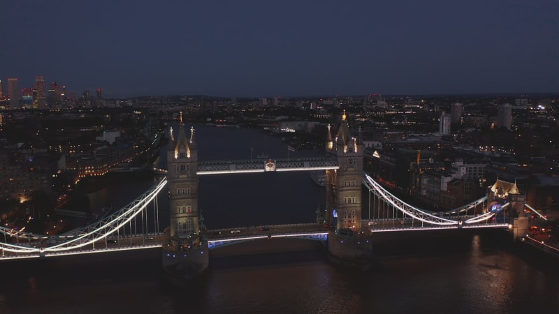 Night fly over Tower Bridge spanning River Thames. Illuminated famous historic landmark. London, UK