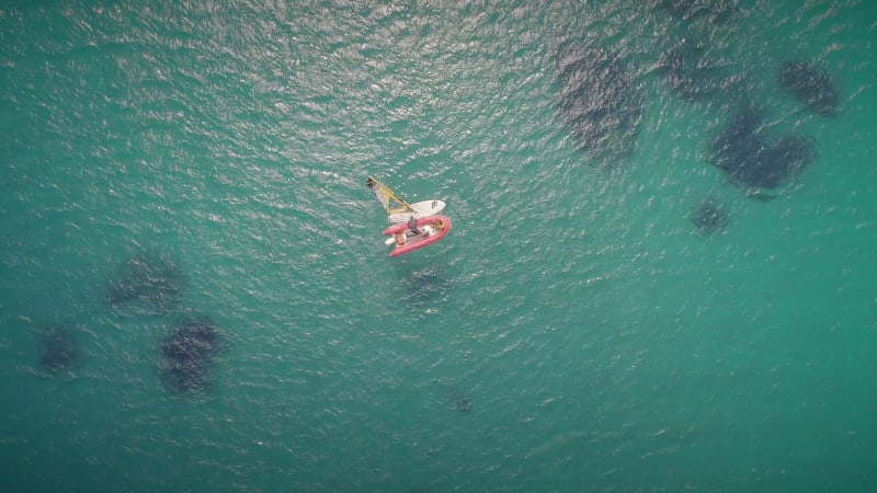 Aerial view of windsurfer and boat in turquoise sea.