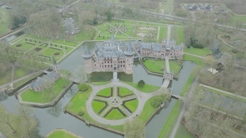 Flying backwards tilting up from a Dutch Castle in Utrecht, The Netherlands between the trees and garden during cloudy fall day