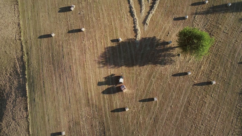 Abstract aerial view of tractor harvesting straw bales in field.