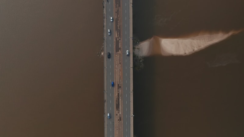 Aerial birds eye overhead top down panning view of wide multilane road bridge with tram tracks in middle. Cars and trams running on bridge and surrounding intersection. Warsaw, Poland