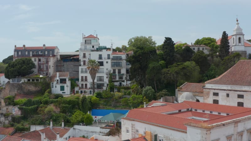 Drone camera following terrain profile and rising over hill. Flying above houses to old Saint George Castle. Revealing city panorama. Lisbon, capital of Portugal.