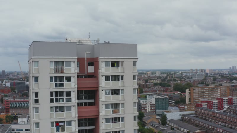 Orbit shot around high rise white apartment building towering above surrounding houses. Modern skyscrapers in background. London, UK