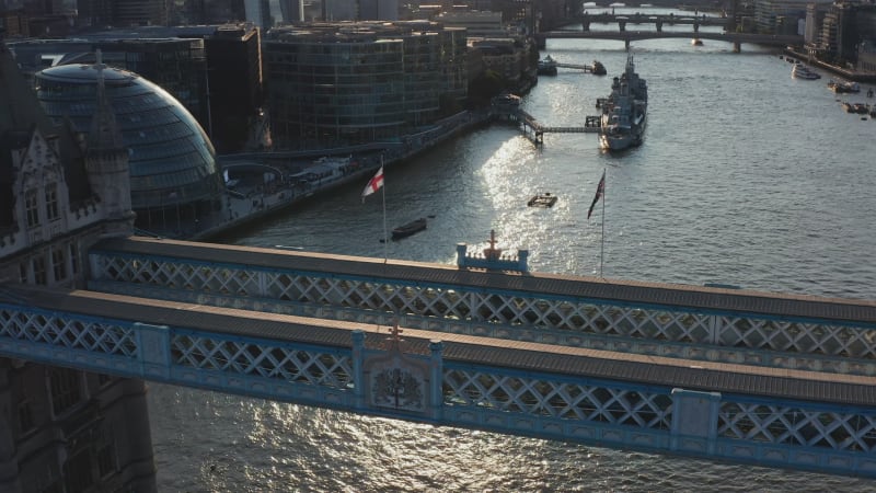 Backwards fly above top walkway of Tower Bridge. Tilt up reveal of bridges across River Thames and Shard skyscraper on south bank. View against sunshine. London, UK