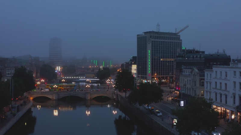 Rising footage of evening misty city. Cars and buses driving on OConnell Bridge. Water surface reflecting lights. Dublin, Ireland