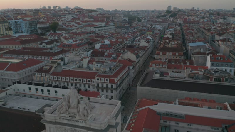 Aerial view of red rooftops of colorful houses in Lisbon city center and  Arco da Rua Augusta monument in traditional European town