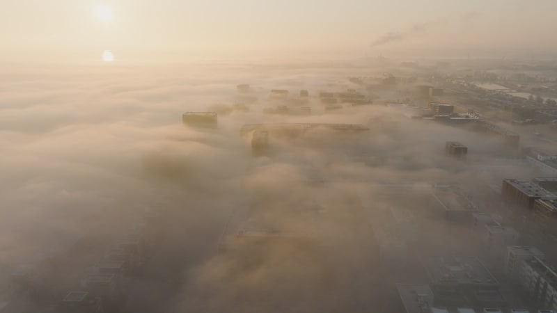 Forwards shot flying out of clouds above the mist packed city and water Amsterdam, The Netherlands during sunrise.