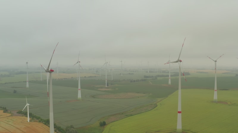 Mehrere Windturbinen auf einem satten gelben Ackerfeld im Nebel, der sich durch die Kraft des Windes dreht und erneuerbare Energie auf grüne, ökologische Weise für den Planeten erzeugt