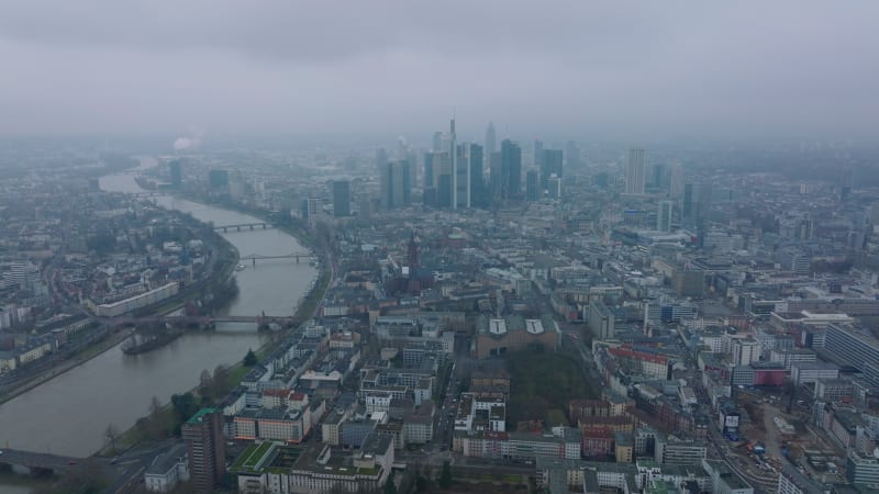 Aerial panoramic footage of large city on hazy day. Wide river flowing through city. Group of modern downtown skyscrapers. Frankfurt am Main, Germany