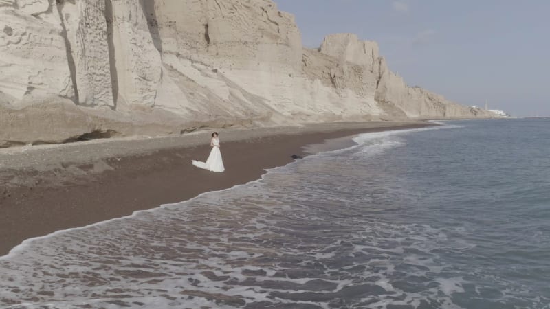 Aerial view of woman with wedding dress on beach Santorini island.