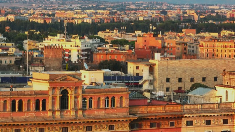 Aerial ascending footage of old buildings in urban borough at sunset. Facades lit by bright low sun. Revealing traffic on railway line. Rome, Italy