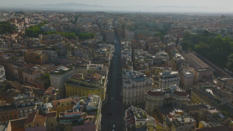 Aerial panoramic footage of historic urban borough. Forwards fly above street and tilt down on Piazza Barberini with Fontana del Tritone. Rome, Italy