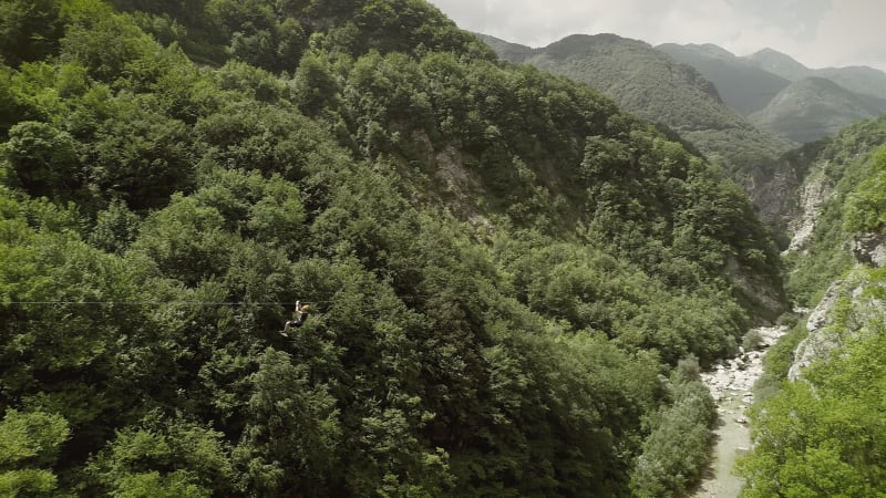 Aerial view of a person riding on zipline flying through the forest.