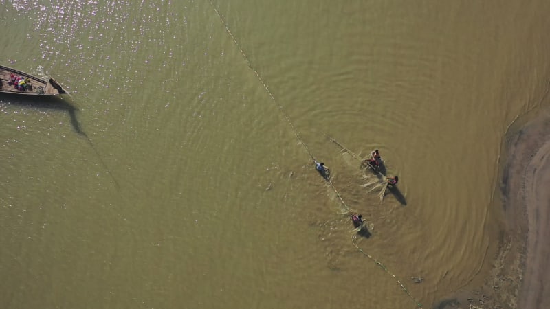 Aerial view of people using large fishing nets along the shoreline on the river, Bangladesh.