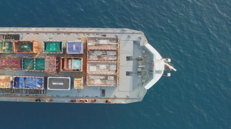 Frachtschiff beladen mit bunten Containern und großen Kisten, das auf See kreuzt.