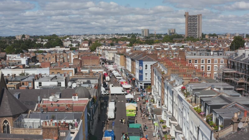 Forwards fly above famous street market on Portobello Road. Aerial view of street with stands offering various products. London, UK