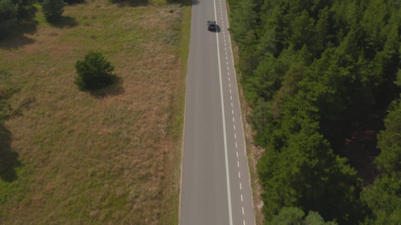 Forwards tracking of car going on straight road in countryside. Tilt up reveal of flat landscape. Cyclist path marked on side of road. Denmark