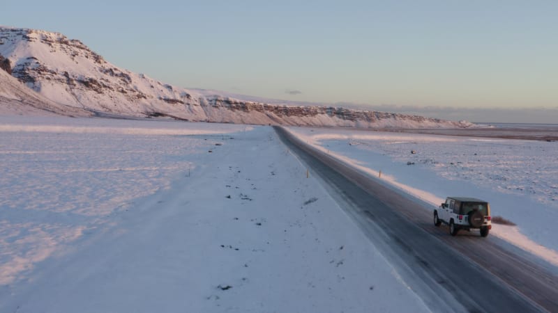 Fliegen neben dem Jeep auf verschneiter Straße in Island bei Sonnenuntergang mit Sonnenflair Winter, Sonne, Arktis