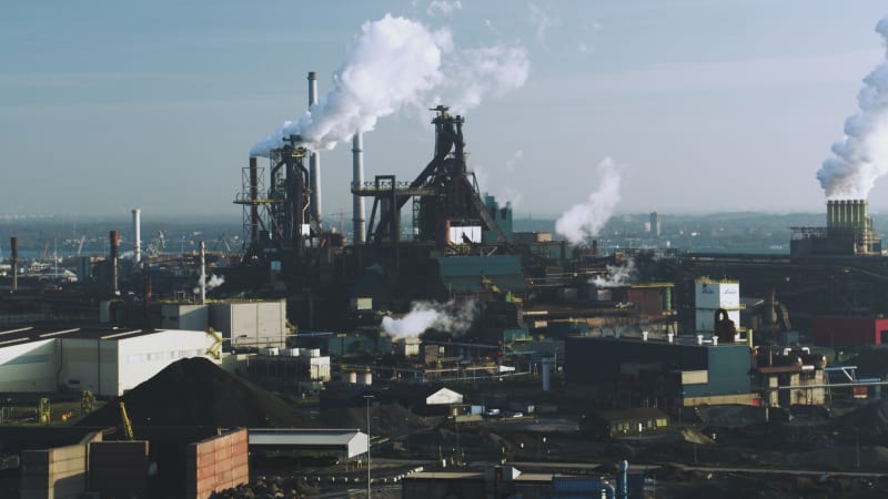 Rotierende Windkraftanlage vor einem Industriekomplex