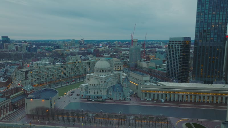 Aerial slide and pan shot of The First Church of Christ with large dome. Sacral landmark surrounding modern downtown skyscraper. City at twilight. Boston, USA