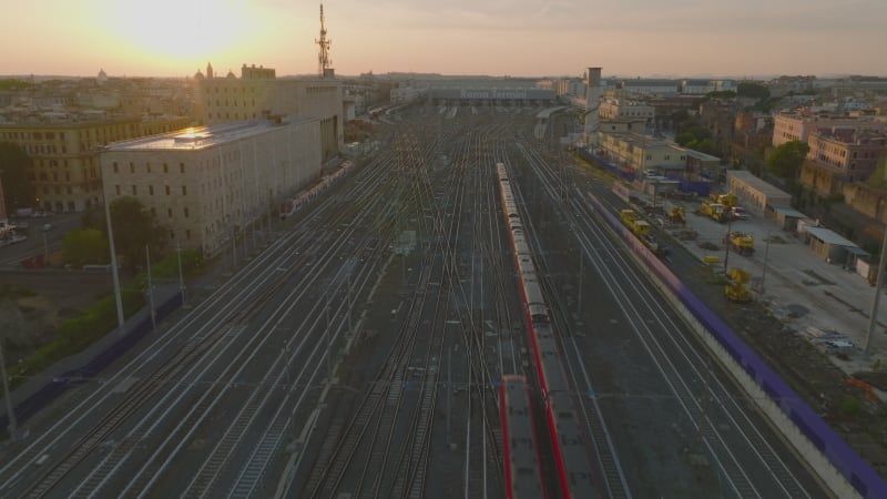 Forwards tracking of passenger train unit heading to central train station, passing by next train moving reverse direction. Aerial view against sunset. Rome, Italy