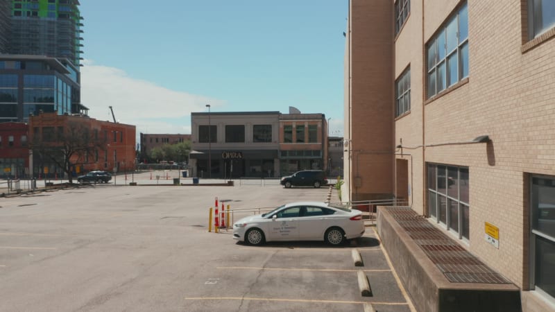 Aufnahmen eines einsamen weißen Personenkraftwagens, der auf einem Parkplatz in der Stadt steht, während eine Drohne leise auf einer Asphaltdrohne landet. Dallas, Texas, Vereinigte Staaten